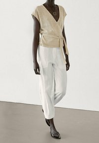 Light beige wrap top with short sleeves and belted waist, paired with loose, white wide-leg pants. Smooth fabric, minimal design.