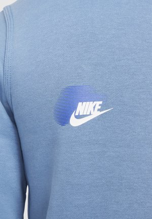 Nike sweatshirt in light blue fabric, featuring a gradient blue logo with white accents on the upper left side. Smooth texture.