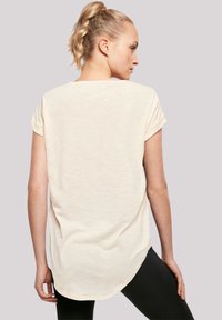 Helles Beige, Kurzarm-T-Shirt mit abgerundetem Saum, strukturiertem Stoff und hochgeschlagenen Ärmeln, getragen mit schwarzen Leggings.