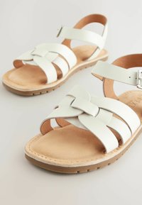 Sandales en cuir blanc avec des brides croisées, une bride de cheville à boucle et une semelle intérieure matelassée couleur tan ; dotées d'une semelle extérieure texturée pour une meilleure adhérence.