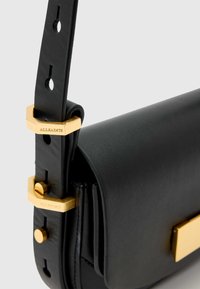 Fekete bőr kézitáska arany díszítéssel, jellegzetes csattal és állítható pánttal, melyen látható lyukak vannak a hosszúság testreszabásához.