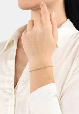Pulsera de cadena de oro con un diseño de eslabones intrincados, descansando sobre una muñeca. El fondo es neutro, destacando los detalles de la pulsera.