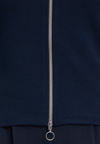 Navy blue zip-up jacket made of textured fabric, featuring a metallic zipper along the center front with a circular pull tab.