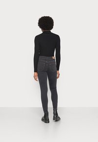 Top negro de manga larga con textura en relieve combinado con unos pantalones vaqueros de tiro alto en gris oscuro, que presentan una silueta ajustada y un sutil detalle en los bolsillos traseros.