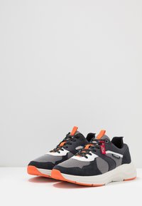 Schwarze und graue Sportschuhe aus Mesh- und Wildledermaterialien, mit orangen Akzenten, einer weißen Sohle und einem strukturierten Schnürdesign.