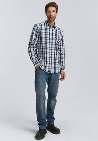 Koszula w kratę zapinana na guziki w kolorach niebieskim, białym i czerwonym; zestawiona z niebieskimi dżinsami i czarnymi butami. Posiada długie rękawy i kołnierzyk.