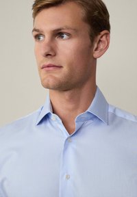 Lichtblauw gestreept overhemden met een scherpe kraag, gemaakt van een gladde stof. Het heeft een slim-fit ontwerp en een klassieke knoopsluiting.