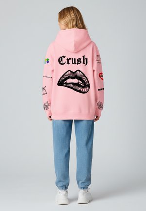 Felpa rosa con una grafica di labbra nere e la scritta "Crush" sul retro, con vari design delle maniche. Abbinata a pantaloni jogger azzurri.