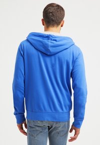 Sudadera azul con capucha, de manga larga, con un bolsillo tipo canguro y puños acanalados. Textura de tela suave y diseño simple.