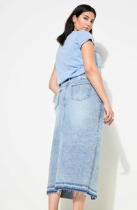 Falda de mezclilla azul claro con dobladillo deshilachado, que cuenta con bolsillos y una cintura alta. Combinada con una blusa de manga corta azul claro.