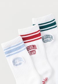 Τρία ζευγάρια λευκές κάλτσες με ριμπ μανσέτες. Το πρώτο έχει ανοιχτό μπλε ρίγες, το δεύτερο έχει κόκκινες ρίγες, και το τρίτο έχει σκούρες πράσινες ρίγες.