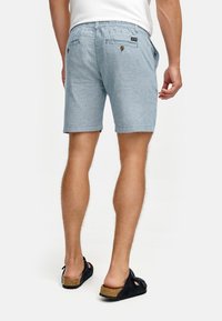 Lichtblauwe chambray shorts met een relaxte fit, zijzakken en twee achterzakken met knoopsluitingen. Draagt samen met zwarte sandalen.