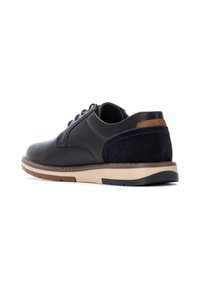 Zapato de cuero negro con acento de gamuza en la parte trasera. Presenta una suela crema con detalles en marrón y azul marino. Diseño con cordones y forma de punta redondeada.