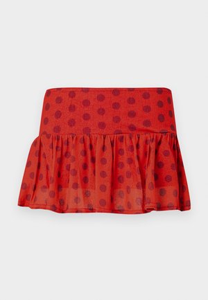 Jupe rouge à volants avec des pois noirs, confectionnée en tissu léger. Elle présente une taille ajustée et un design à couches.