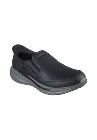 Scarpa nera slip-on con tomaia sintetica liscia, tallone testurizzato e suola grigia flessibile, con branding minimalista sul lato.
