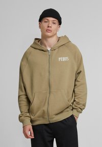 Khaki zip-up hoodie with a large front pocket and ribbed cuffs. Features a white printed logo "PEQUS" on the left chest. Soft fabric texture.