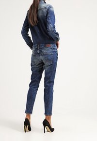 Jeansjacka och jeansoutfit i medelblå tvätt. Jeans har slim fit med fickor; kombinerat med svarta högklackade skor.