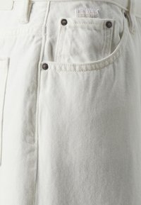Shorts en denim blanc avec un tissu texturé, poches avant avec des rivets métalliques contrastants et une étiquette logo près de la taille.