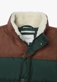 Chaqueta marrón y verde con un diseño acolchado, cuello forrado de sherpa, herrajes de metal y cierre de cremallera. La etiqueta es visible en el interior.