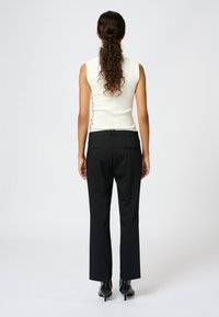 Biała bluzka bez rękawów i czarne, dopasowane spodnie o prostym kroju. Spodnie mają pasek w talii i dwie tylne kieszenie. Widoczne czarne szpiczaste szpilki.