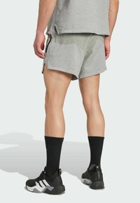 Shorts de sport gris avec des fentes latérales, assortis avec des chaussettes noires jusqu'aux genoux et des chaussures noires avec des accents blancs et des semelles texturées.