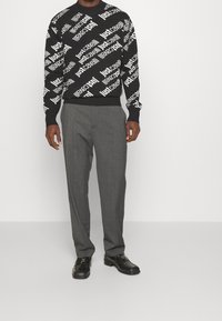 Svart tröja med "justcavalli"-text i vitt, ribbade ärmslut, kombinerad med grå skräddarsydda byxor och svarta finskor.