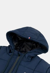 Giacca a cappuccio navy con design trapuntato, cordini regolabili e interno in satin con un piccolo accento tricolore sul cappuccio.