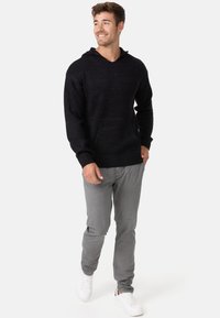 Sudadera negra con capucha, de diseño de punto texturizado y bolsillo frontal, combinada con pantalones gris claro y zapatillas blancas.