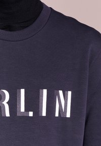 Felpa navy con colletto a coste, con scritta audace in bianco che spell "BERLINO". Il tessuto sembra testurizzato e morbido.