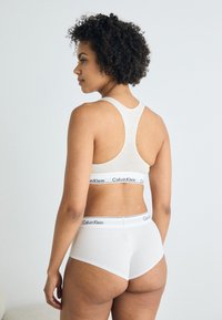 Hvit bomull sports-bh med racerback-design og Calvin Klein-logo langs kanten, kombinert med matchende hvite hipster-truser.