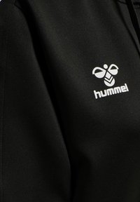 Schwarzer Hoodie mit glatter Textur, versehen mit einem weißen "hummel"-Logo und einer Biene-Grafik auf der Vorderseite. Einfaches, modernes Design.