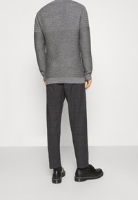 Šedý svetr s texturou a dlouhými rukávy, kombinovaný s tmavými kalhotami s kostkovaným vzorem. Černé boty s kontrastním detailem na podrážce.