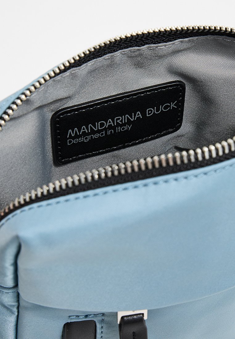 Blauer Nylonbeutel Innenraum mit grauem Futter, silbernem Reißverschluss und schwarzem Etikett mit der Aufschrift "Mandarina Duck, Designed in Italy." Verfügt über ein elegantes Design.