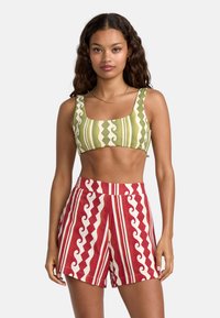 Crop top vert et blanc à motifs avec un col carré, associé à un short rouge comportant des motifs en zigzag et des rayures blanches. Tissus décontractés et légers.