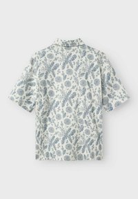 Camisa de manga corta en blanco, con un patrón floral azul, cuello y corte relajado. Hecha de tela ligera, con textura suave.
