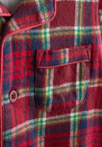 Rød, grøn, gul og marineblå ternet uldstof med en knap og en lille lomme med klap syet på forsiden.