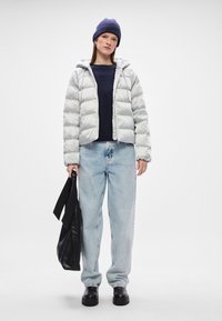 Duhovni kaput u svijetlosivoj boji, sa kapuljačom, u kombinaciji s tamnoplave džemperom, širokim plavim trapericama, crnim čizmama i crnom torbom.