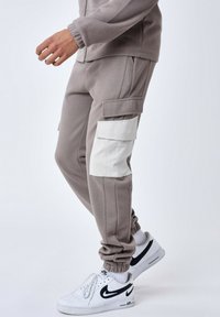 Grijze joggings met cargozakken, voorzien van een witte panel aan de zijkant. Elastische boorden en een gestructureerde afwerking verbeteren het comfort en de pasvorm.