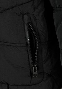 Melnā pūkaino džaketu audumam ir teksturēta virsma ar rāvējslēdzēju kabatu. Rāvējslēdzējam ir melns vilkšanas rokturis, un tas ir pastiprināts malās.