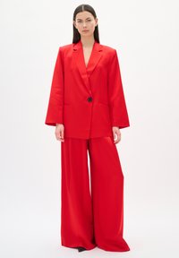 Blazer rojo con mangas anchas, cierre de un solo botón; pantalones de pierna ancha a juego; textura suave; diseño minimalista; fondo liso.