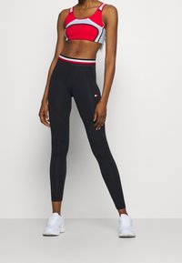 Czerwona i szara sportowa góra z dekoltem w serek i cienkimi ramiączkami, zestawiona z czarnymi legginsami o wysokim stanie z logo i kontrastowym pasem.