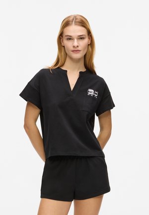 Čierny bavlnený top s krátkym rukávom, výstrihom do V a náprsným vreckom s grafickým motívom. Dopĺňa ho pár čiernych krátkych nohavíc v rovnakom štýle.