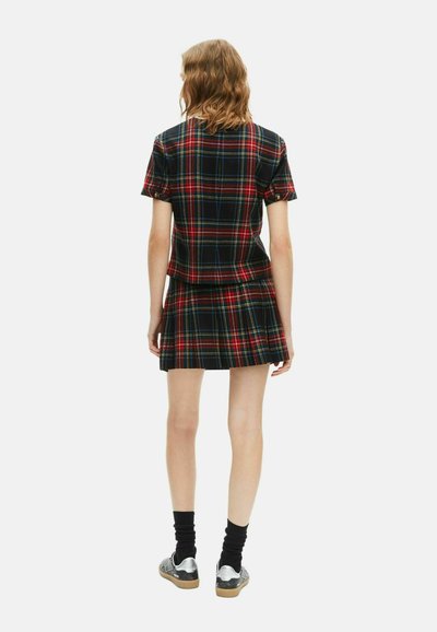 Sorte ternet to-delt outfit med korte ærmer og en plisseret nederdel. Har røde, blå og grønne linjer. Båret med sorte sokker og sølvfarvede sko.