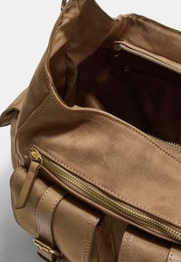 Sac à main en suede marron doux avec une poche zippée à l'avant, des sangles en cuir à boucle et un compartiment principal ouvert montrant une poche zippée intérieure.