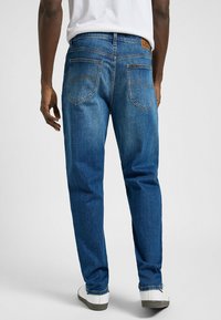 Jeans de mezclilla azul con un corte relajado, bolsillos traseros con detalles de costura y una etiqueta de marca de cuero en la cinturilla.