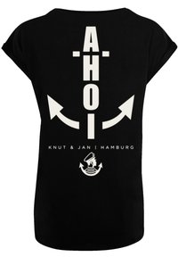 Schwarzes T-Shirt mit weißem grafischem Text "AHOI" sowie Pfeilen und einem Matrosen-Icon, zusätzlich mit dem Text "KNUT & JAN | HAMBURG" am unteren Rand.