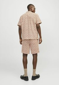 Chemise à manches courtes imprimée et short assorti en marron clair avec un motif floral répétitif. Le tissu semble lisse, avec une coupe décontractée.