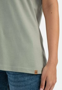 Lichtgroene katoenen t-shirt met een afgeronde zoom en een klein geweven label aan de onderkant. Gepaarde met blauwe denim spijkerbroek.