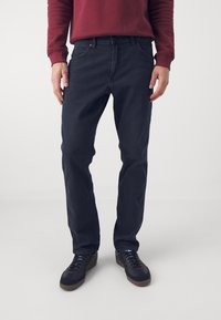 Blugi din denim de culoare albastru închis, cu o croială dreaptă, având un design clasic cu cinci buzunare și detalii subtile de cusătură.