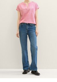 Lys pink kortærmet bluse med V-udskæring og rullede ærmer, parret med blå mellemhøj talje lige ben cowboybukser og sorte sko.